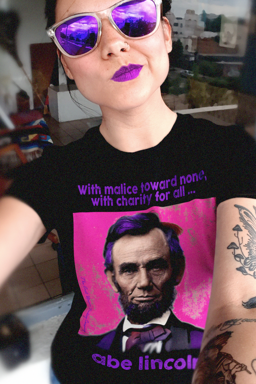 Hip woman in purple sunglasses wearing Relaxed Fit Women’s Tee with American Punk Abraham Lincoln — “With malice toward none, with charity for all.” From his Second Inaugural Address. Great gift for American radicals. 