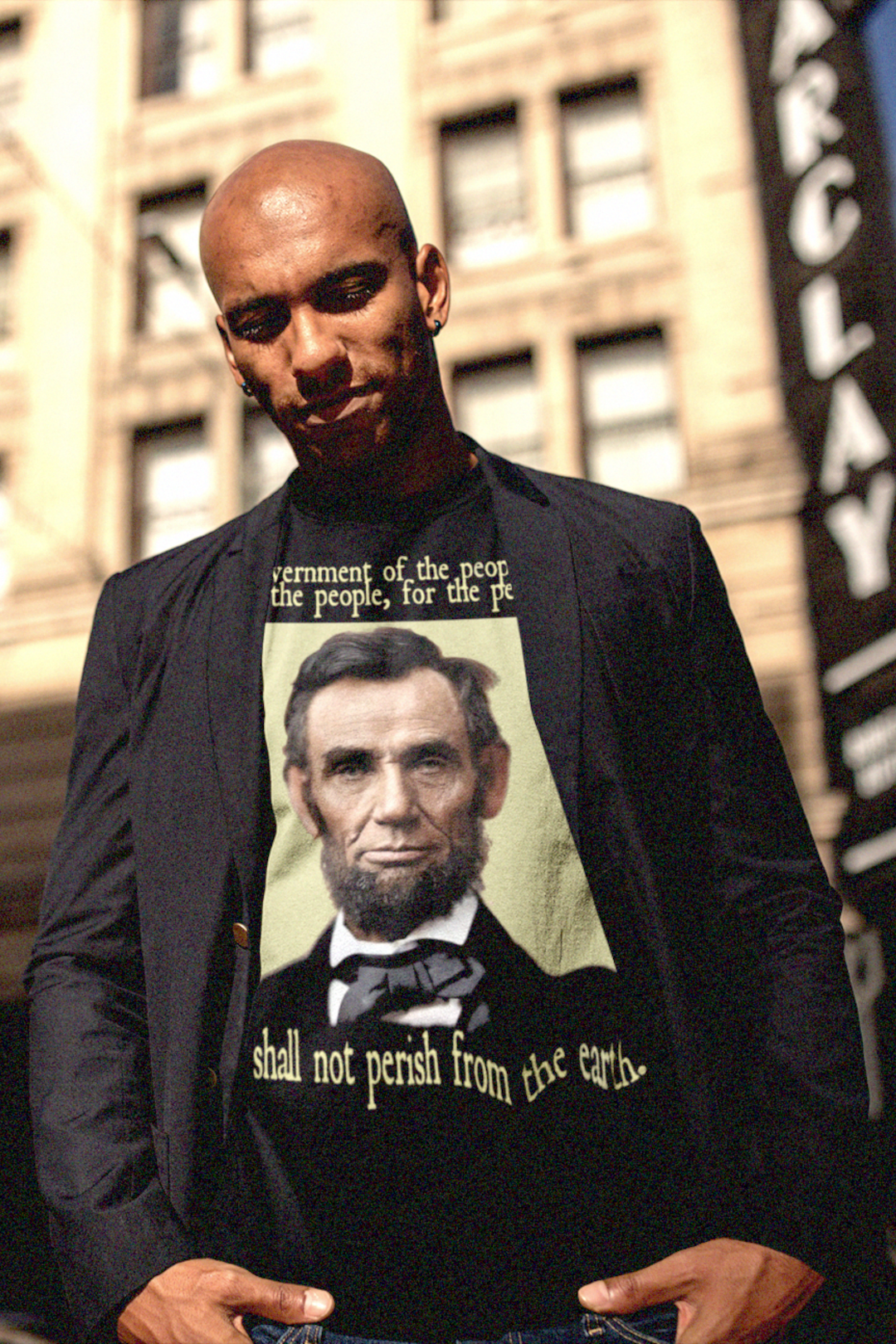 Bald Black man in a sport coat wearing a t-shirt depicting Abraham Lincoln: Government of the people, by the people, and for the people shall not perish from the earth. 

Abraham Lincoln wasn’t a saint dropped from the heavens—he was a messy, pragmatic politician shaped by the rough-and-tumble Free Soil movement and the hard edges of frontier republicanism. 

Perfect gift for the presidential history buff in your life or the radical pragmatist. Bella+Canvas 3001 Basic Black T-Shirt #EUTC