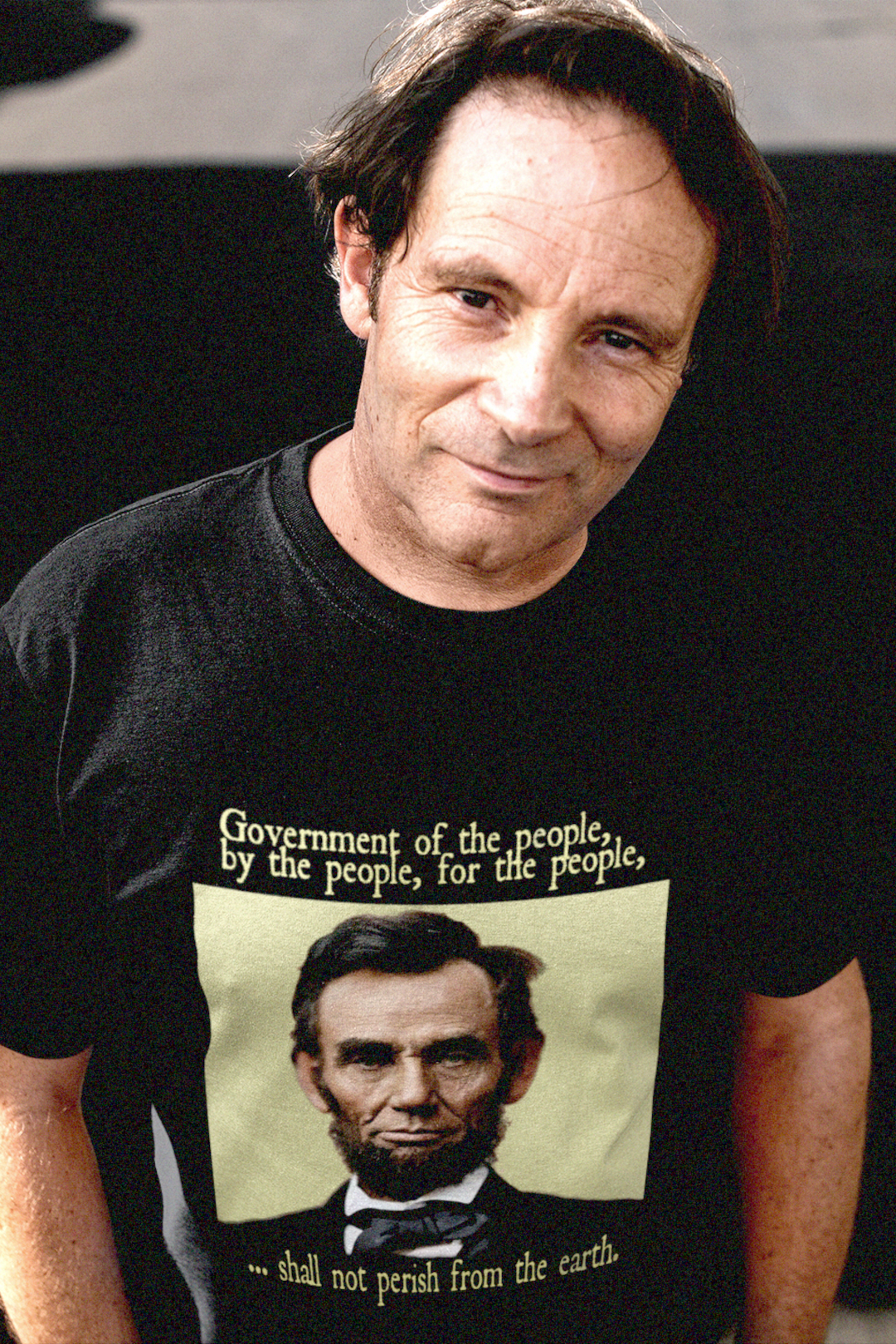 Middle aged White guy in the street wearing a t-shirt depicting Abraham Lincoln: Government of the people, by the people, and for the people shall not perish from the earth. 

Abraham Lincoln wasn’t a saint dropped from the heavens—he was a messy, pragmatic politician shaped by the rough-and-tumble Free Soil movement and the hard edges of frontier republicanism. 

Perfect gift for the presidential history buff in your life or the radical pragmatist. Bella+Canvas 3001 Basic Black T-Shirt #EUTC