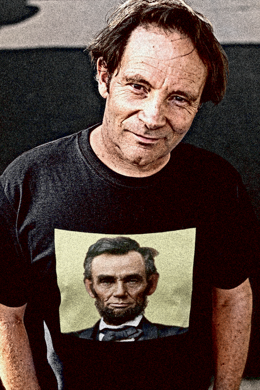 Tough middle aged White guy looking up from street wearing a Basic Black T-Shirt with khaki colorized portrait of Abraham Lincoln. From his Second Inaugural Address, delivered near the end of the Civil War, Lincoln’s words capture the nation’s moral high point amid its deepest wound. Great gift for American radicals and history buffs. Bella+Canvas 3001 Basic T-Shirt #EUTC
