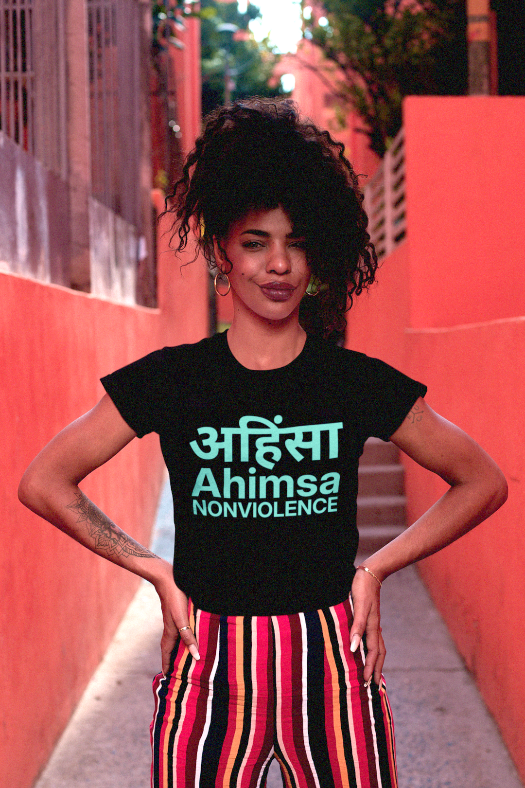 A woman with a kinky afro and multi-colored striped trousers in a black relaxed fit women's tee: AHIMSA — The Principle of Nonviolence
Mahatma Gandhi transformed Ahimsa अहिंसा into a political force, extending it from private virtue to public resistance. 
Perfect gift for the activist and nonviolent protester in your life. Bella+Canvas 6400 Women’s Relaxed Tee #EUTC