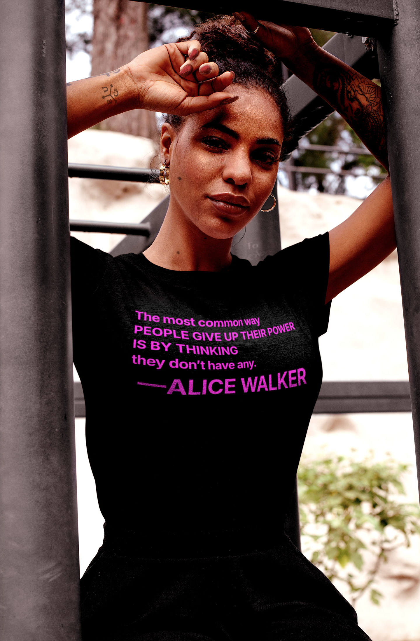 Defiant Black woman sitting on a jungle gym wearing a Black Relaxed Fit Women's Tee with the Alice Walker quote “The most common way people give up their power is by thinking they don't have any.” —Poet, novelist, and activist Alice Walker (b. 1944) distills the essence of empowerment in this call to awareness. Great gift for your book club friend or the feminist activist in your life. Cotton Bella+Canvas 6400 #EUTC