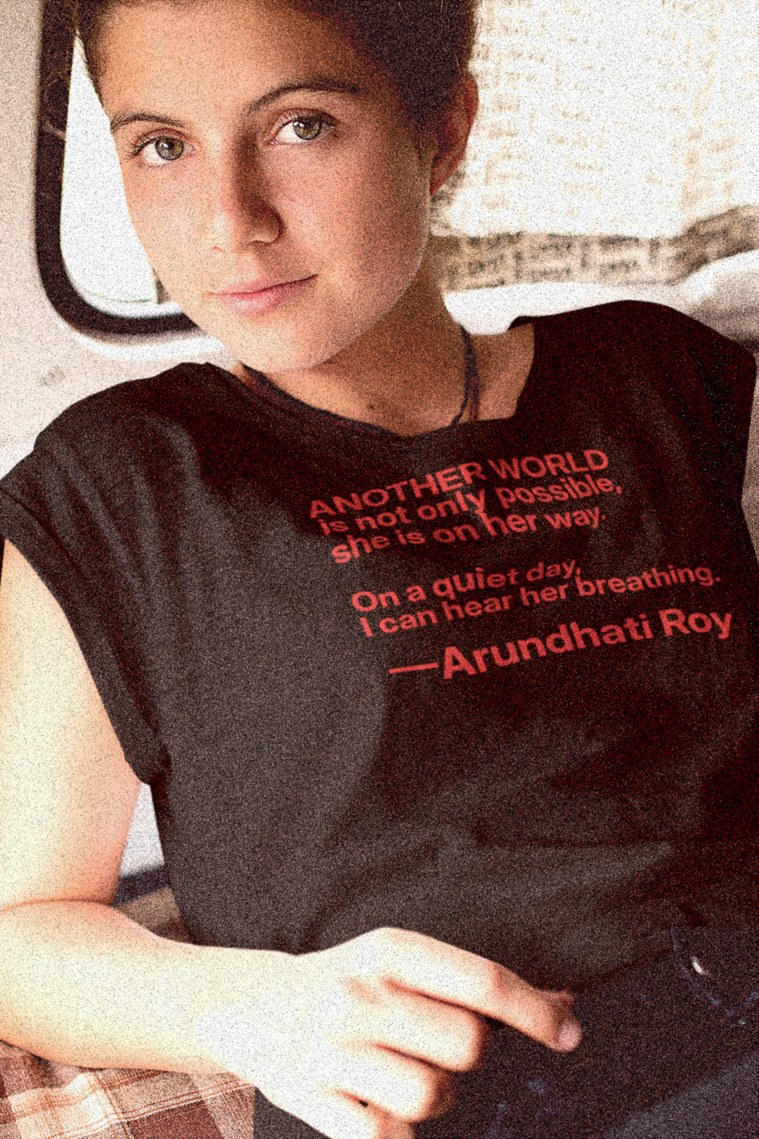 Slim White woman in the back of a VW Micro Bus wearing a Basic Black T-Shirt with quote: “Another world is not only possible. On a quiet day, I can hear her breathing.” —Arundhati Roy Booker Prize-winning author of The God of Small Things, is a fearless voice for social justice, environmental protection, and human rights. Bella+Canvas 6400 #EUTC