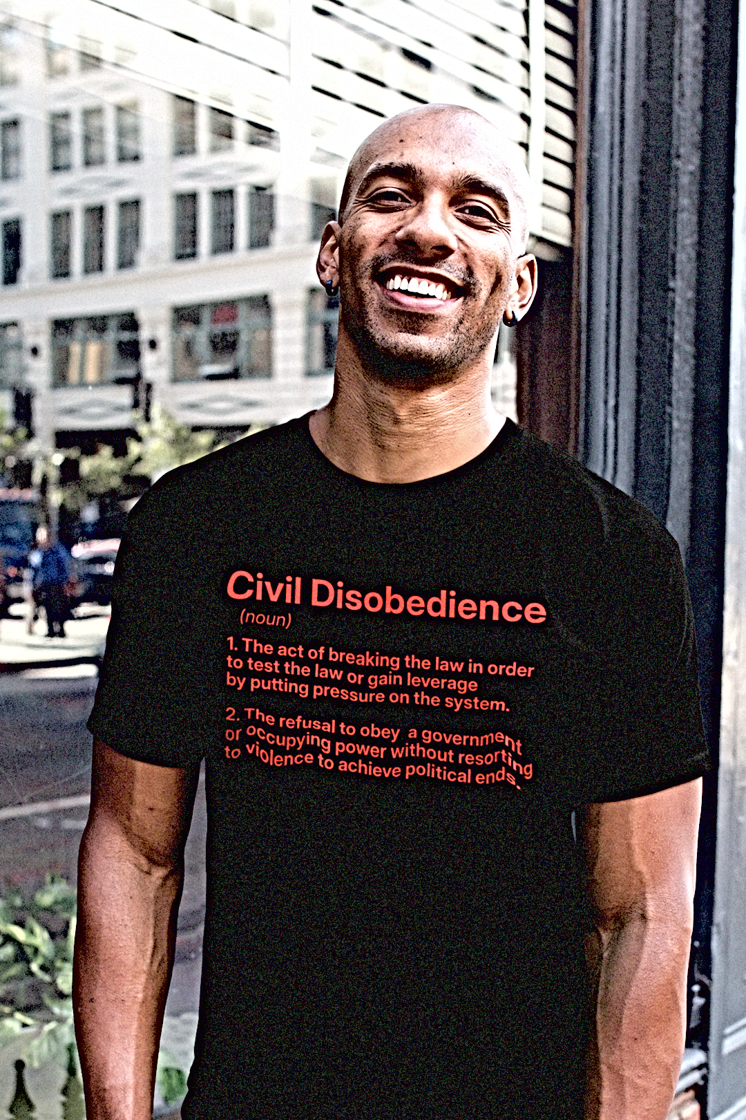Muscular bald Black man on a city street wearing a Basic Black T-Shirt with the definition for CIVIL DISOBEDIENCE (noun) 1. The act of breaking the law in order to test the law or gain leverage by putting pressure on the system. 2. The refusal to obey a government or occupying power without resorting to violence to achieve political ends. 

Perfect gift for the political outlaw in your life. Protesters and activists. Cotton Bella+Canvas 3001 #EUTC