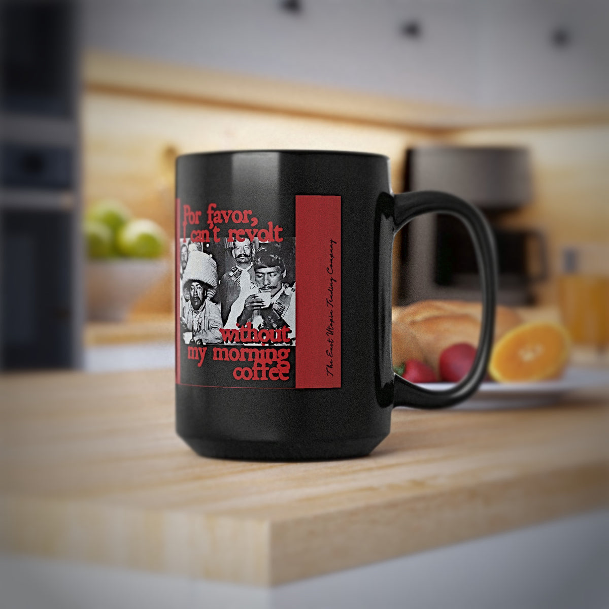 A black ceramic coffee mug with  "Por Favor, I can't revolt without my morning coffee" mug featuring Mexican Revolutionaries at Sanborn's placed on a wooden cutting board in a blurred kitchen setting.