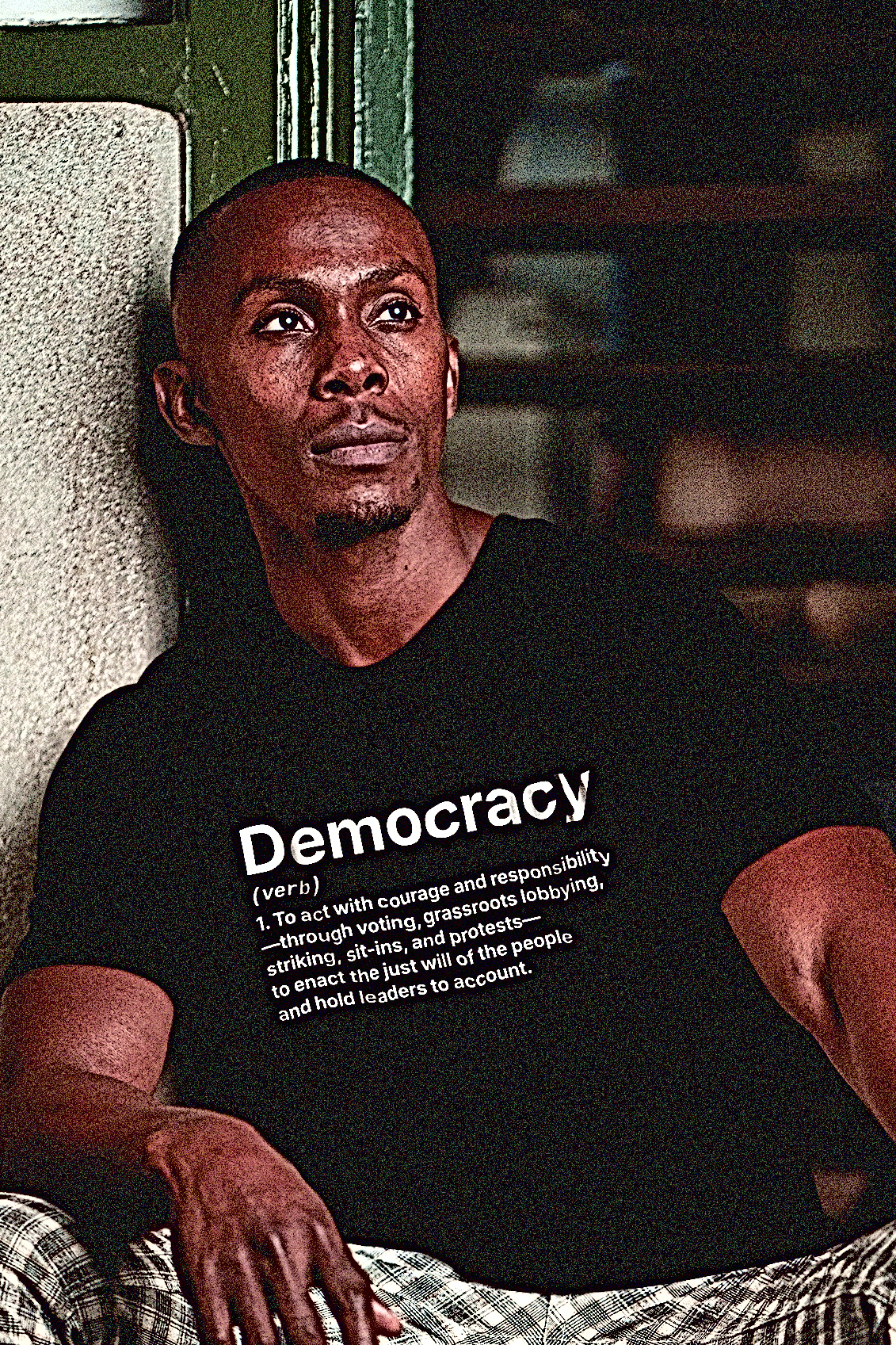 Tough, stylish Black man wearing a Basic Black T-Shirt with the definition for DEMOCRACY (verb)  1. To act with courage and responsibility —through voting, grassroots lobbying, striking, sit-ins, and protests — to enact the just will of the people and hold leaders to account. | Cotton Bella+Canvas 3001 #EUTC