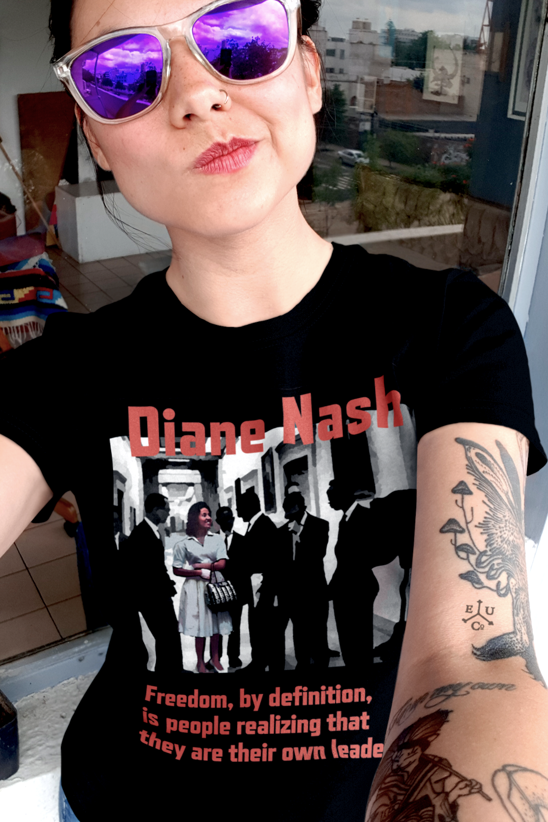 Asian American woman with tattoos and purple reflector sunglasses wearing a Black Relaxed Fit Women's T-Shirt:  Diane Nash was the strategist the movement needed but history almost forgot. As a student leader in SNCC, she organized sit-ins, freedom rides, and voter registration drives with a clarity and toughness that left older male leaders scrambling to keep up. Perfect gift of feminist civil rights activists. Cotton Bella+Canvas 6400 #EUTC