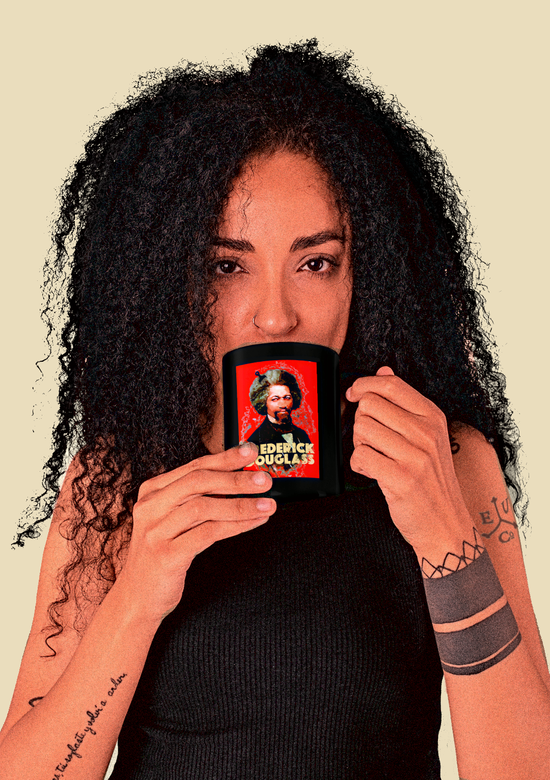 A woman with voluminous curly black hair holds a black mug in front of her face. The mug features a red retro graphic print of FREDERICK DOUGLASS. 