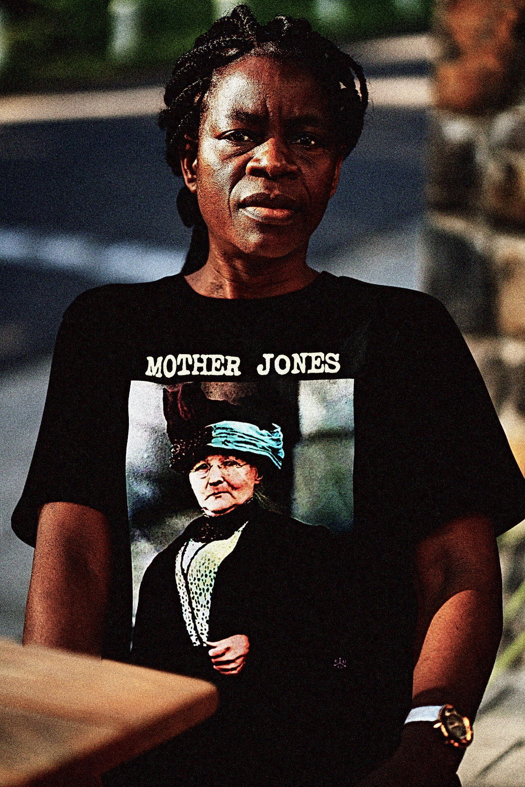 A  older Black female union activist with long braids sitting at an outdoor cafe wearing a Basic Black T-Shirt: Mother Jones, fearless labor organizer who fought for miners, children, and the dignity of working people. Mary “Mother” Jones was called the most dangerous woman in America—and she wore the title proudly.
Perfect gift for the union organizer or anarcho-syndicalist in your life. Cotton Bella+Canvas 3001 #EUTC