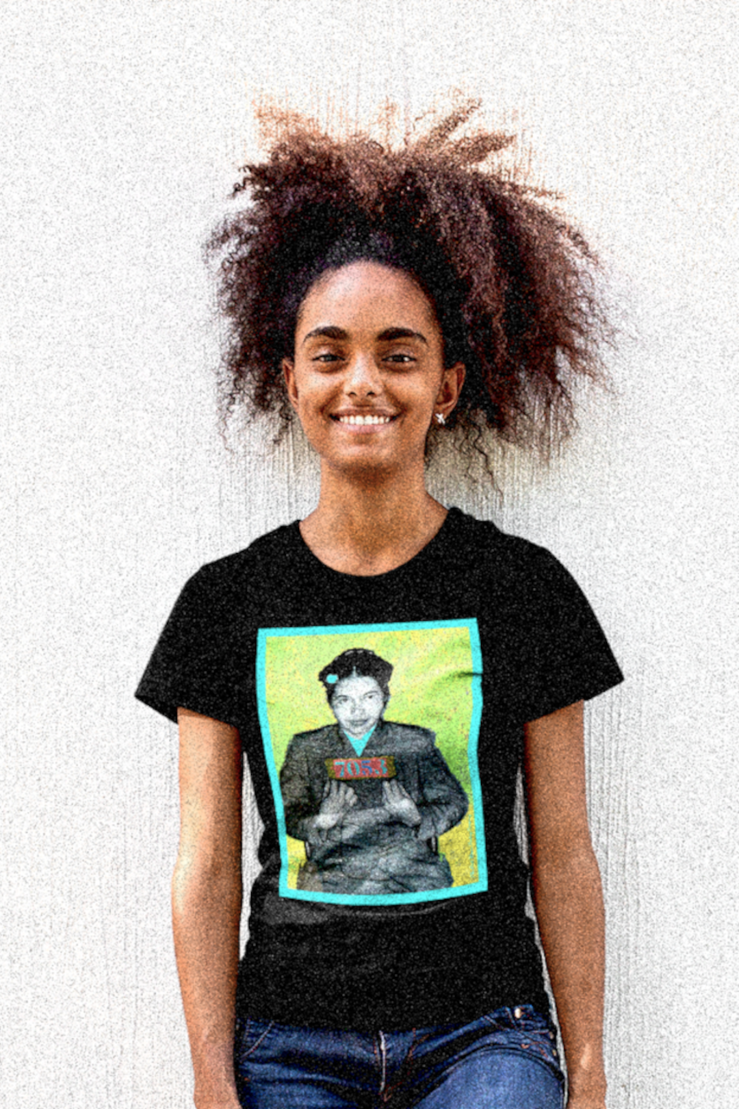 Cool, thin Black woman with large natural afro casually pulled back wearing a basic black t-shirt depicting the mugshot of Rosa Parks, whose quiet defiance sparked the Montgomery Bus Boycott and galvanized the movement. Forget the myth of the tired seamstress—Rosa Parks was a trained activist who knew exactly what she was doing when she refused to give up her seat. Perfect gift for the feminist civil rights activist in your life. Bella+Canvas 3001 #EUTC