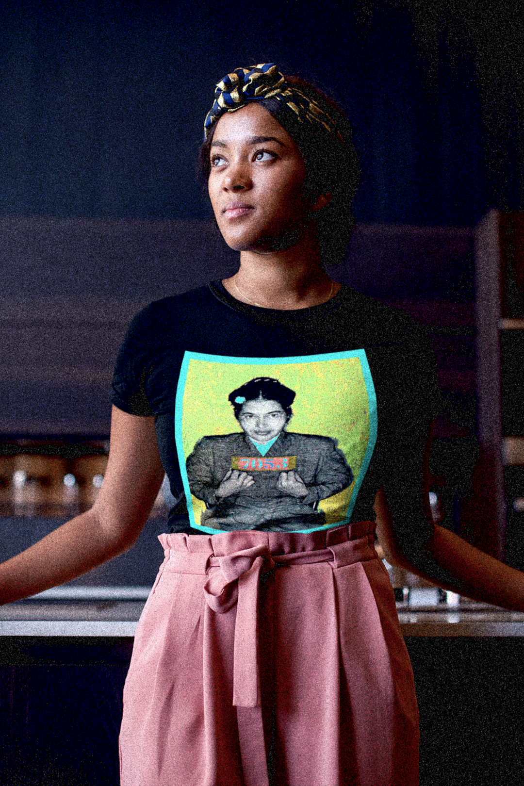 Stylish Black woman with a head scarf and peach pants wearing a relaxed fit women's tee depicting the mugshot of Rosa Parks, whose quiet defiance sparked the Montgomery Bus Boycott and galvanized the movement. Forget the myth of the tired seamstress—Rosa Parks was a trained activist who knew exactly what she was doing when she refused to give up her seat. Perfect gift for the feminist civil rights activist in your life. Bella+Canvas Women’s Relaxed Tee 6400  #EUTC 