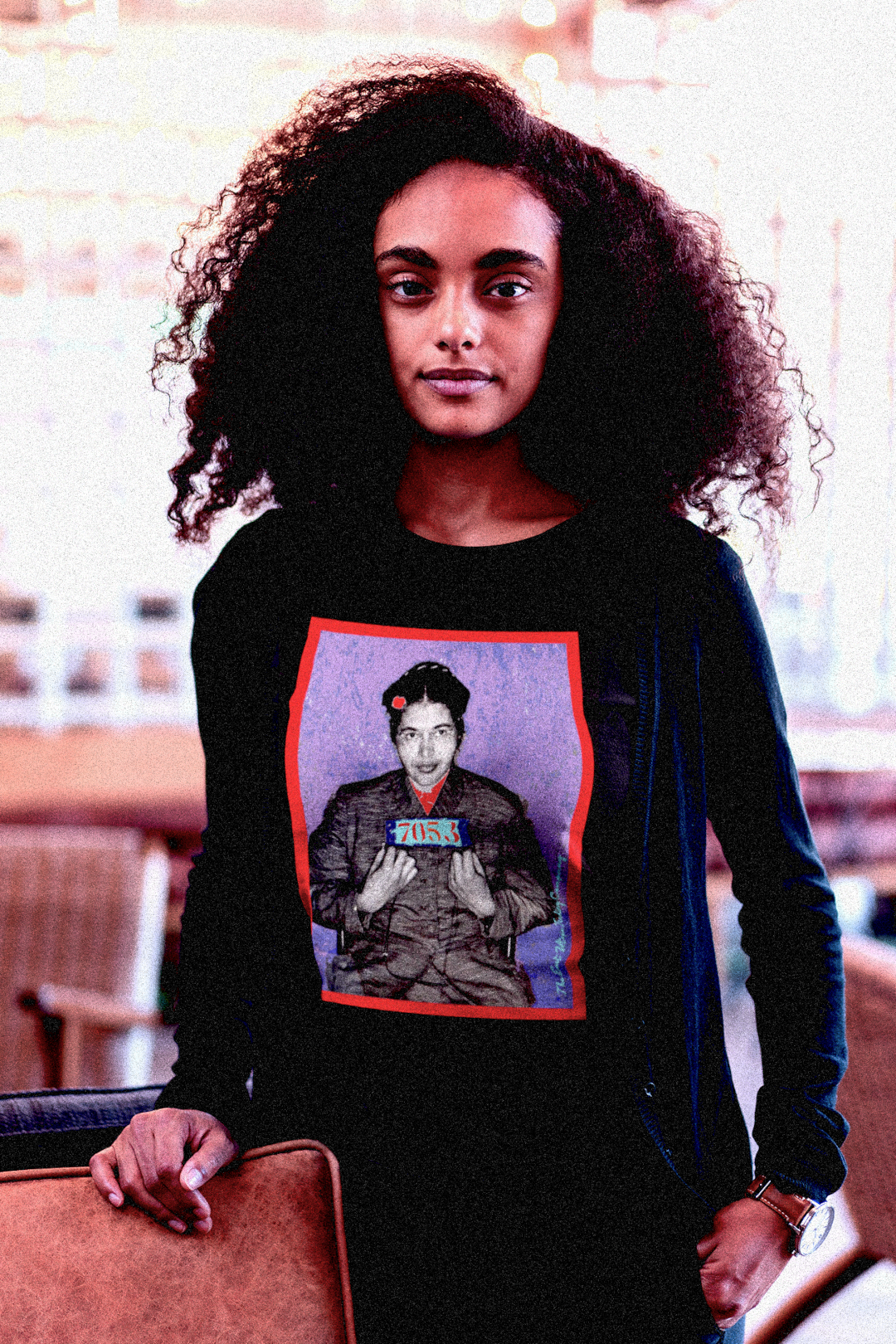 Intellectual Black woman with large natural afro in a college lounge wearing a Black Long Sleeve Jersey depicting the mugshot of Rosa Parks, whose quiet defiance sparked the Montgomery Bus Boycott and galvanized the movement. Forget the myth of the tired seamstress—Rosa Parks was a trained activist who knew exactly what she was doing when she refused to give up her seat. Perfect gift for the feminist civil rights activist in your life. Bella+Canvas 3501  #EUTC