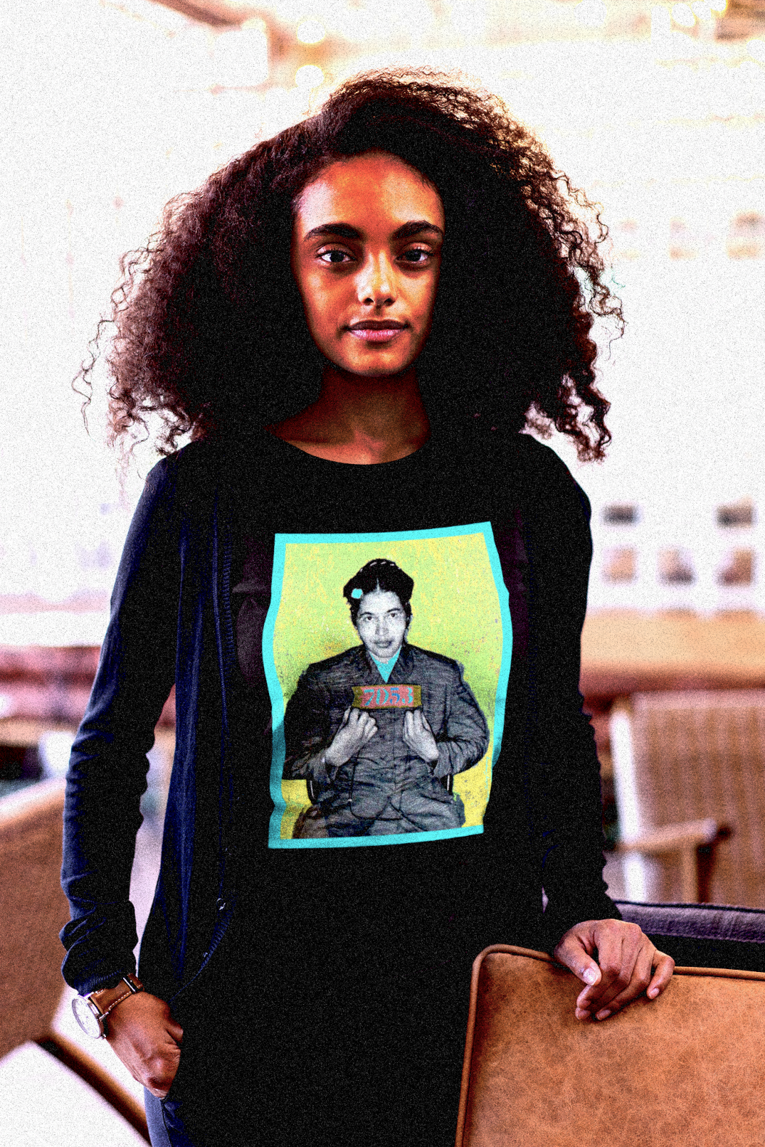 Intellectual Black woman with a big natural afro in a college lounge wearing a black Long Sleeve Jersey depicting the mugshot of Rosa Parks, whose quiet defiance sparked the Montgomery Bus Boycott and galvanized the movement. Forget the myth of the tired seamstress—Rosa Parks was a trained activist who knew exactly what she was doing when she refused to give up her seat. Perfect gift for the feminist civil rights activist in your life. Bella+Canvas 3501  #EUTC 