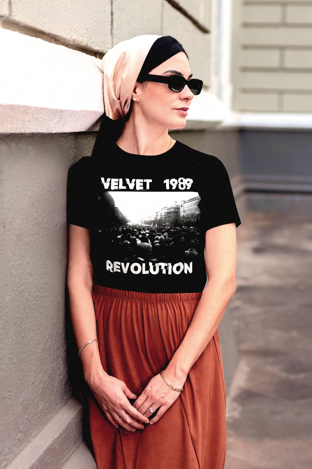 Stylish woman grad student wearing a black t-shirt with 'Velvet 1989 Revolution' text and graphic, standing against a wall. The perfect gift for the democracy activist in your life. 