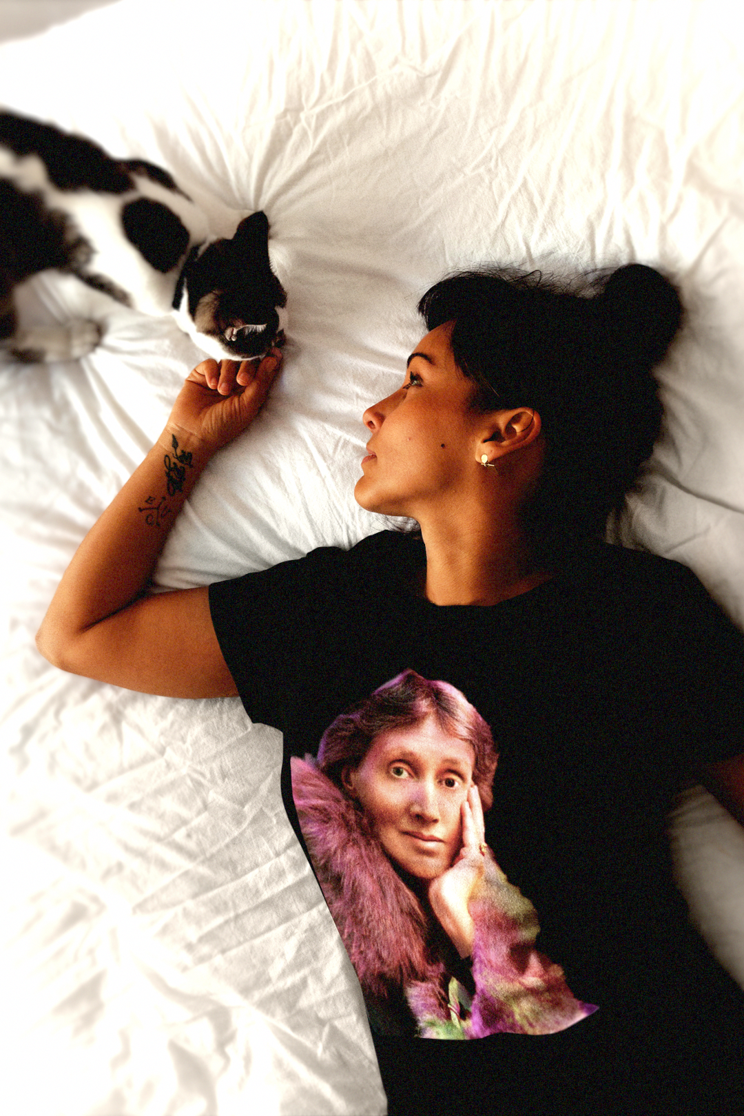 A woman in bed with her cat wearing a relaxed fit women's tee of a technicolor Virginia Woolf. She made literature new—stream-of-consciousness, fractured time, inner lives spilling across the page. Quality cotton tee. Perfect gift for the lover of literature in your life. Bella+Canvas Women’s Relaxed Tee 6400 #EUTC