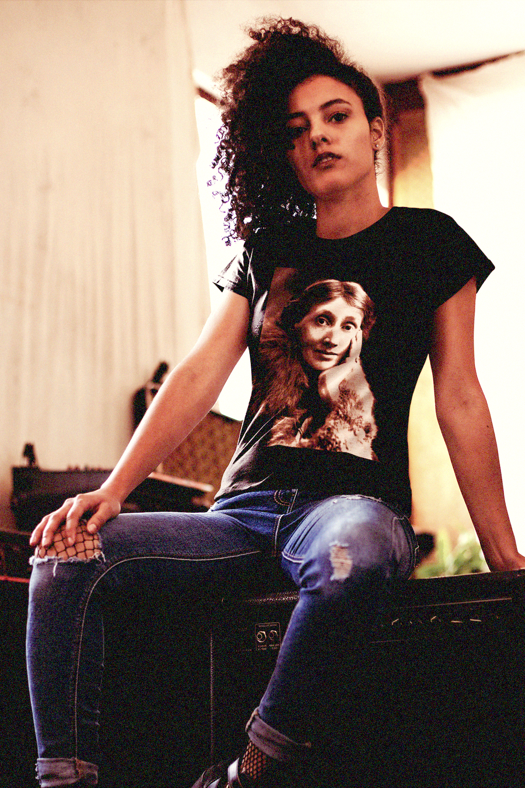 Kinky haired woman sitting on amps wearing a relaxed fit women's Tee with a sepia portrait of Virginia Woolf. She made literature new—stream-of-consciousness, fractured time, inner lives spilling across the page. With novels like Mrs. Dalloway and To the Lighthouse, she redefined modernism not as escape but as immersion. Photo show fit and style. Perfect gift for your book club fit or the English major in your life. #EUTC