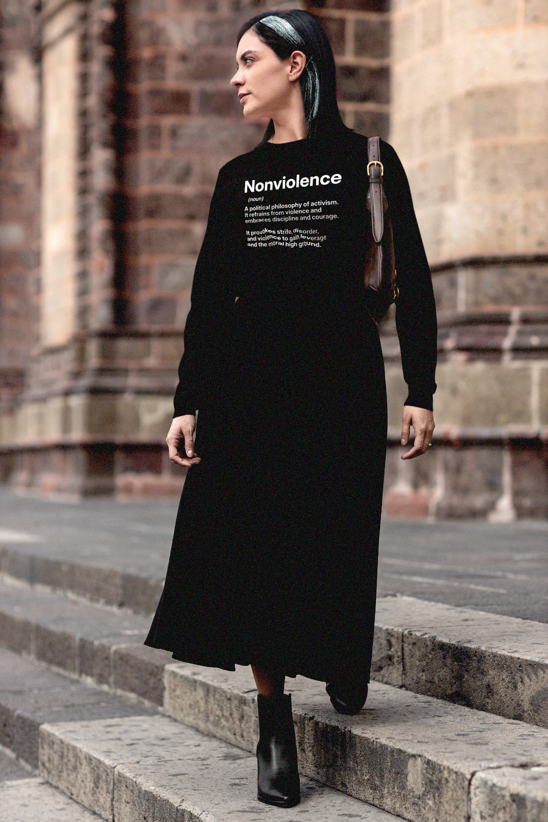 Gothesque female grad student walking across campus wearing a NONVIOLENCE: Quality long sleeve jersey with a text design featuring an activist definition: It refrains from violence and embraces discipline and courage. It provokes strife, disorder, and violence to gain leverage and the moral high ground. Perfect gift for the activist in your life. Quality Bella+Canvas Jersey 3501 #EUTC